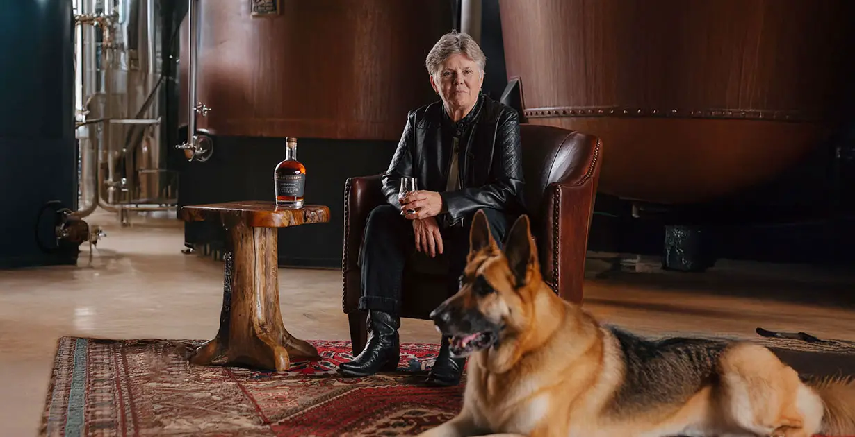 Marlene Holmes sitting in the distillery with a glass of Milam & Greene Whiskey 